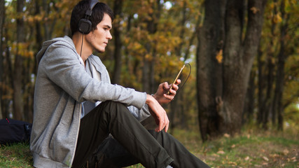 A young man in headphones enjoys a warm autumn day in the Park. Copy space