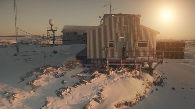 Close-up Vernadsky base and man. Antarctica aerial drone view flight. Fast shot Antarctic snow covered landscape. Camp, base building with walking man. Sunset polar sky. Permafrost. 4k footage.
