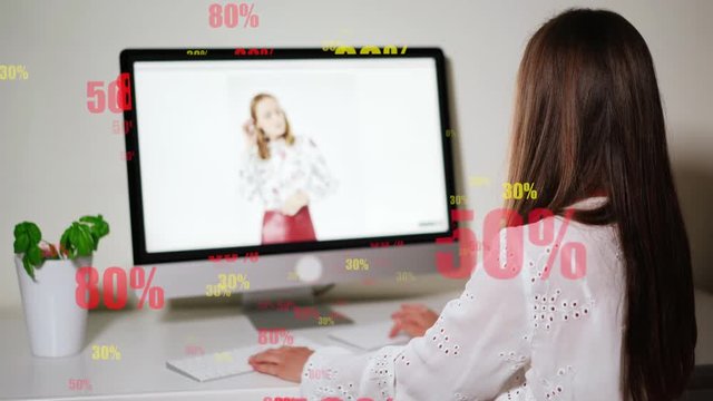 Brunette female sitting in front of computer screen in office and surfing in the internet. Girl making purchases online using discount coupon