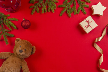 Christmas composition. Teddy bear, fir tree branches, christmas decorations and present gift box on red background