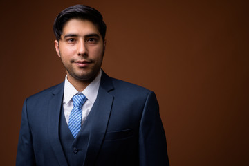 Young handsome Iranian businessman against brown background