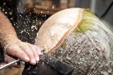 wood working man cuts rotating piecee of timber on turnery machine