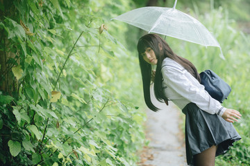 Portrait of Asian school girl walking with umbrella at  nature walkway on raining