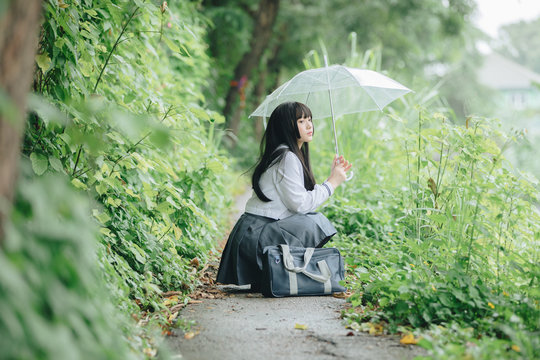 Portrait of Asian school girl walking with umbrella at  nature walkway on raining