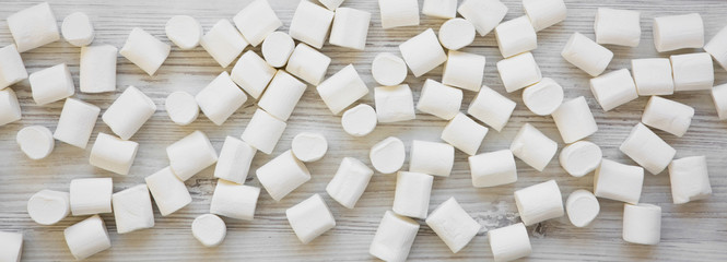 Sweet white marshmallows on a white wooden table, overhead view. Flat lay, from above, top view. Close-up.