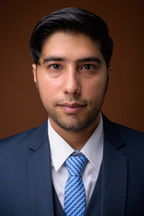 Young handsome Iranian businessman against brown background