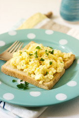 Simple classic breakfast of bread toast and scrambled eggs with parsley.