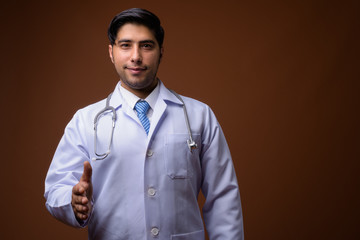 Young handsome Iranian man doctor against brown background