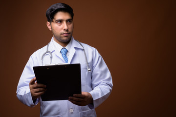 Young handsome Iranian man doctor against brown background