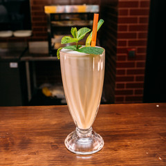 a glass of beautiful bright cocktail on a wooden surface decorated with fruits, berries, leaf of mint and basil at bar counter background
