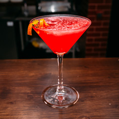a glass of beautiful bright cocktail on a wooden surface decorated with fruits, berries, leaf of mint and basil at bar counter background