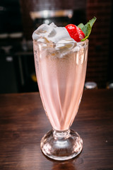 a glass of beautiful bright cocktail on a wooden surface decorated with fruits, berries, leaf of mint and basil at bar counter background