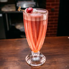 a glass of beautiful bright cocktail on a wooden surface decorated with fruits, berries, leaf of mint and basil at bar counter background