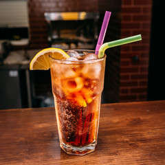 a glass of beautiful bright cocktail on a wooden surface decorated with fruits, berries, leaf of mint and basil at bar counter background