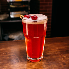 a glass of beautiful bright cocktail on a wooden surface decorated with fruits, berries, leaf of mint and basil at bar counter background