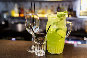a glass of beautiful bright cocktail on a wooden surface decorated with fruits, berries, leaf of mint and basil at bar counter background