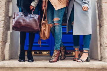 Three women wearing stylish shoes and accessories outdoors. Autumn fashion concept. Ladies holding female handbags