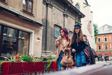 Obraz premium Outdoor shot of young women walking on city street. and having coffee. Friends talking and having fun