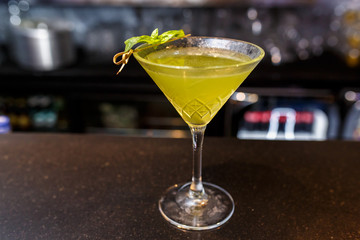 a glass of beautiful bright cocktail on a wooden surface decorated with fruits, berries, leaf of mint and basil at bar counter background