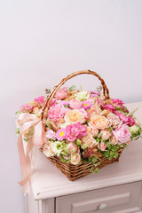flowers arrangement with various of colors in wicker basket on pink table. beautiful spring bouquet. bright room, white wall. copy space