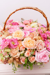 Fototapeta na wymiar flowers arrangement with various of colors in wicker basket on pink table. beautiful spring bouquet. bright room, white wall. copy space