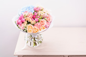 beautiful spring bouquet. flowers arrangement with various of colors in glass vase on pink table. bright room, white wall. copy space