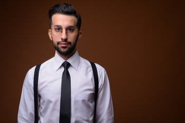 Young handsome bearded Iranian businessman against brown backgro