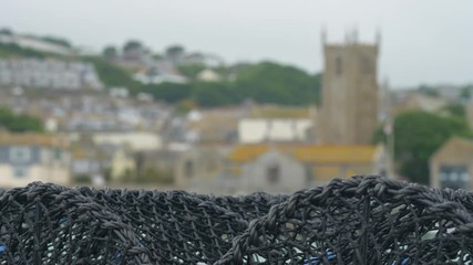 Focus pull shot of lobster traps and St Ives harbour, and church beyond.
