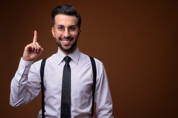 Young handsome bearded Iranian businessman against brown backgro