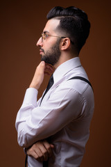 Young handsome bearded Iranian businessman against brown backgro