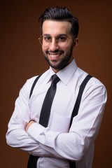 Young handsome bearded Iranian businessman against brown backgro