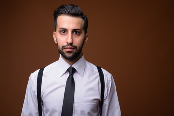 Young handsome bearded Iranian businessman against brown backgro