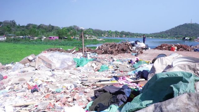 Kid standing on pile of trash in landfill. South American poor neighborhood next to river.