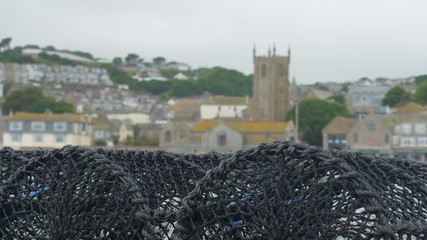 Focus pull shot of lobster pots and St Andrews Church and St Ives harbour beyond.
