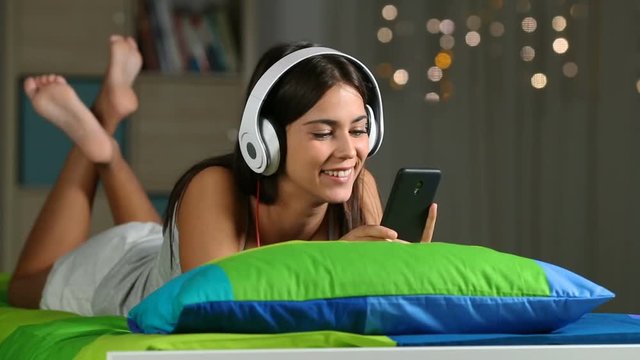 Teen listening to music with phone and headphones at home sitting on a couch in the living room