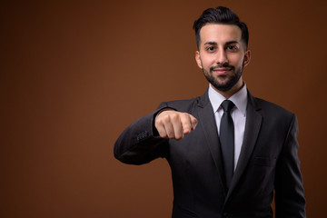 Young handsome bearded Iranian businessman against brown backgro