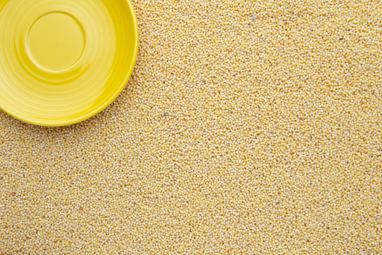 Yellow dry uncooked millet background and yellow plate on it, top view, vertical