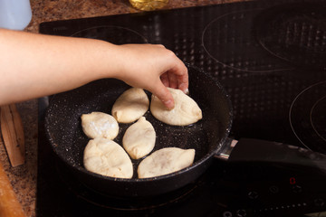 Meat pies, pan-fried in boiling oil. Female hand puts small raw pies in a frying pan with hot oil