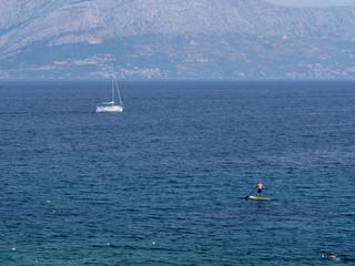 Coastline at Adriatic sea, Croatia. A swimmer, a man on a paddling board and sailing boat at the sea. Sunny summer day.