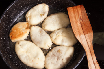 Meat pies, pan-fried in boiling oil. small raw pies in a frying pan with hot oil. wooden spatula