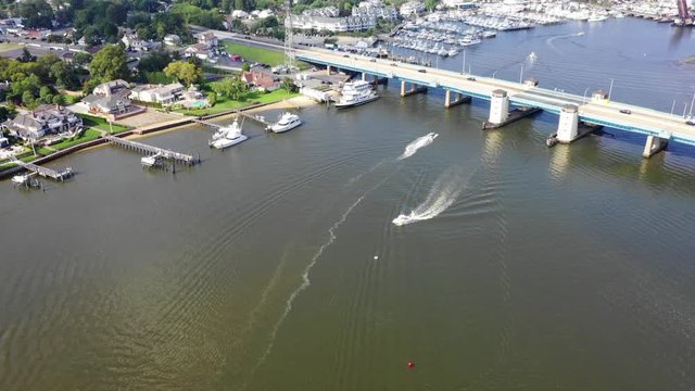 Aerial drone shot over a river leading out to the ocean with boats and a busy bridge with cars in Brielle, New Jersey.