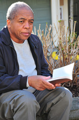 African american male reading a book outside.