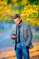 Fototapeta premium Young man with mobile phone in autumn season alley.