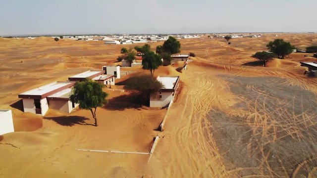 7m and rising aerial, moving through a sand covered deserted town. Camera moves up while panning from the horizon to overhead view.