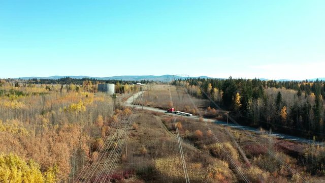 A cinematic, moving, aerial view of some power lines crossing over a back road with an orange / red truck driving past during the autumn season.