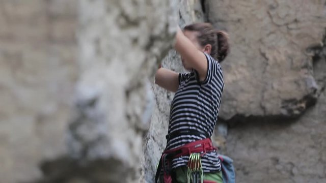 side view of woman rock climber in bright green pants climbing on the cliff. rock climber climbs on a rocky wall. woman making hard move