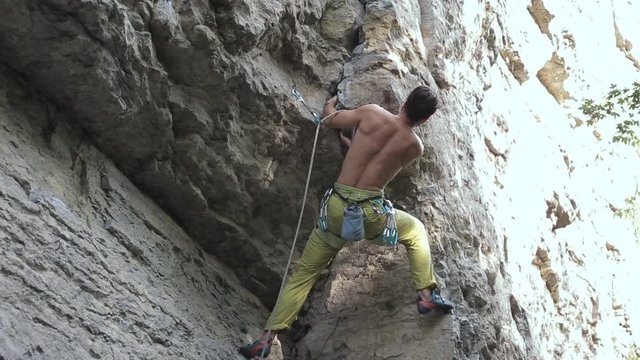 muscular man rock climber in bright yellow pants climbing the challenging route on the cliff. strong bearded rock climber climbs on a rocky wall