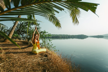 A woman is meditating by the river with a garland of flowers around her neck. In the foreground...