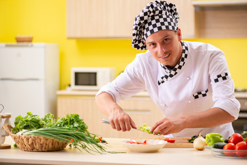 Young professional cook preparing salad at kitchen