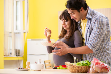 Obraz na płótnie Canvas Man and pregnant woman preparing salad in kitchen 